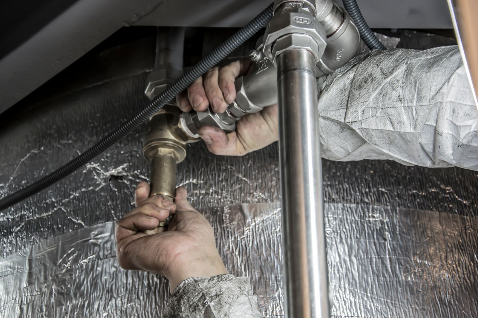 Hands fitting steel pipework indoors