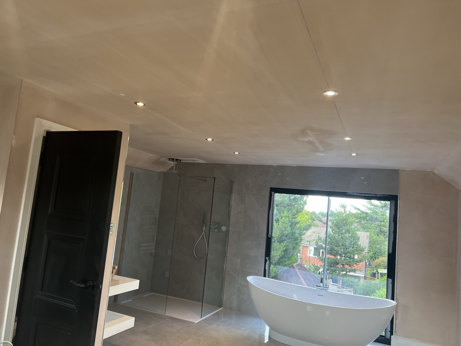 Downlights set out across a finished bathroom ceiling, wired and positioned around the shower enclosure and freestanding bath.