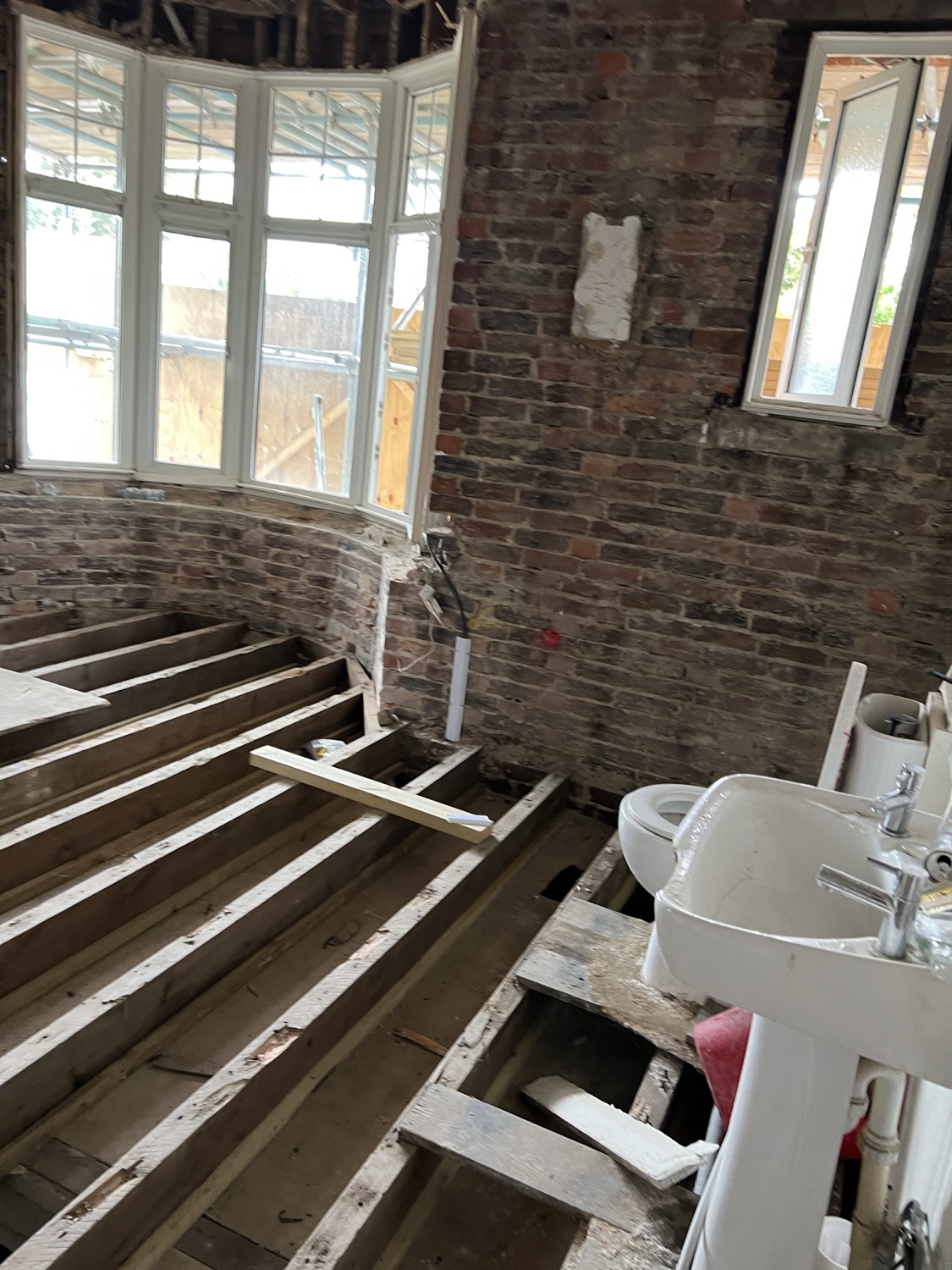 A bathroom back to bare joists and brickwork — the stage where pipe runs and cabling get set out properly before anything is boarded over.